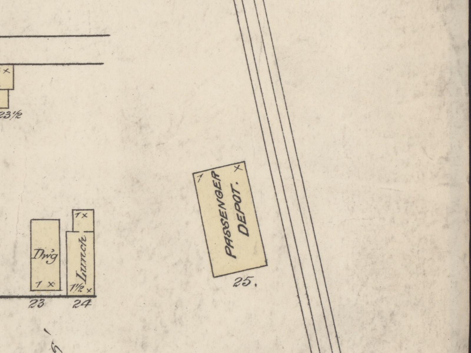 A detail of an 1883 fire insurance map, printed in black line with buildings washed in pale yellow. A rectangular building set at an angle to the sheet is lettered PASSENGER DEPOT and numbered 25. Four parallel lines run diagonally past it from top to bottom, the railroad. To the west stand two small buildings lettered Dwg and Lunch, numbered 23 and 24, and part of a scale bar shows at the lower left corner.
